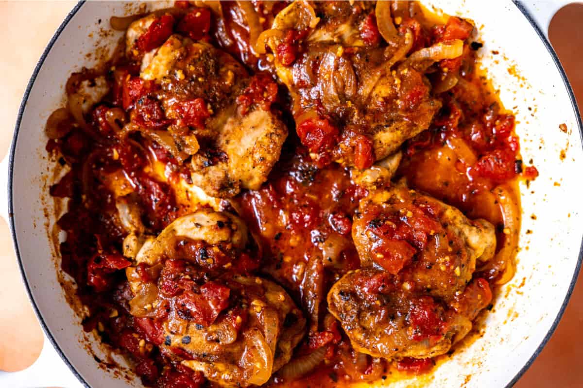 Slow roasting chicken thighs in a skillet with tomatoes and onion. 