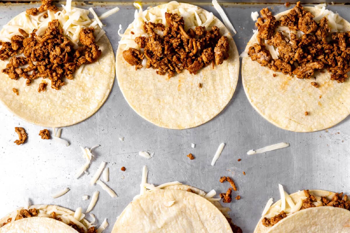 Corn tortillas on a sheet pan topped with ground turkey taco meat and grated cheese.