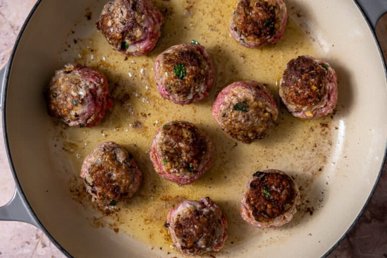 Swedish meatballs in a skillet searing in oil.