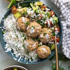 Bowl of rice, cilantro lime chicken meatballs and tomato avocado salad drizzled with crema and crumbled queso fresco.