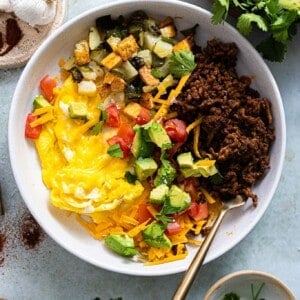 Breakfast bowl with egg, chorizo, potatoes and topped with avocado and tomato.