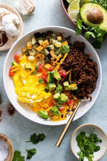 Breakfast bowl with egg, chorizo, potatoes and topped with avocado and tomato.