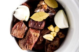 Seared chuck roast in a slow cooker with onion, garlic, and bay leaves.
