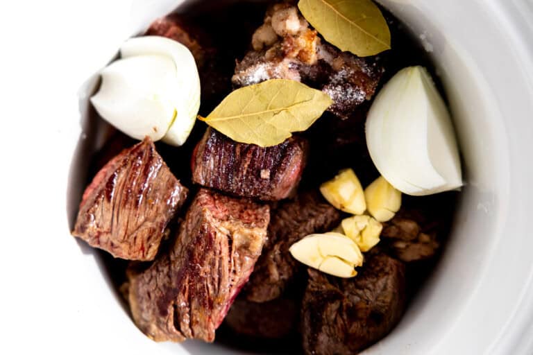 Seared chuck roast in a slow cooker with onion, garlic, and bay leaves.