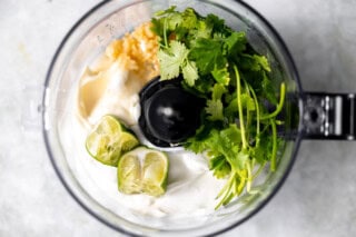 Ingredients needed to make cilantro lime sauce in a food processor.