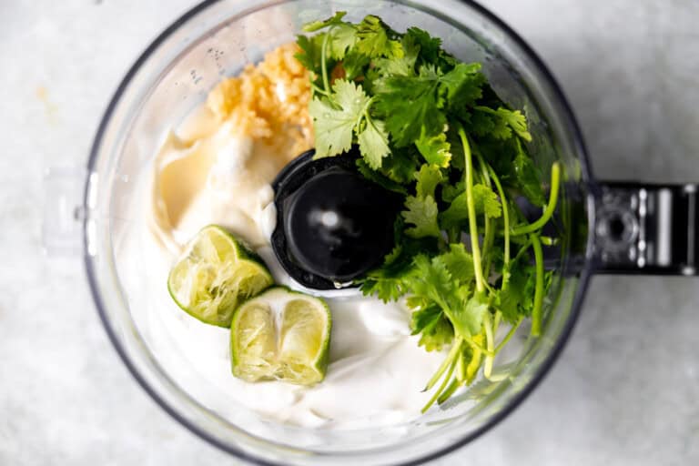 Ingredients needed to make cilantro lime sauce in a food processor.