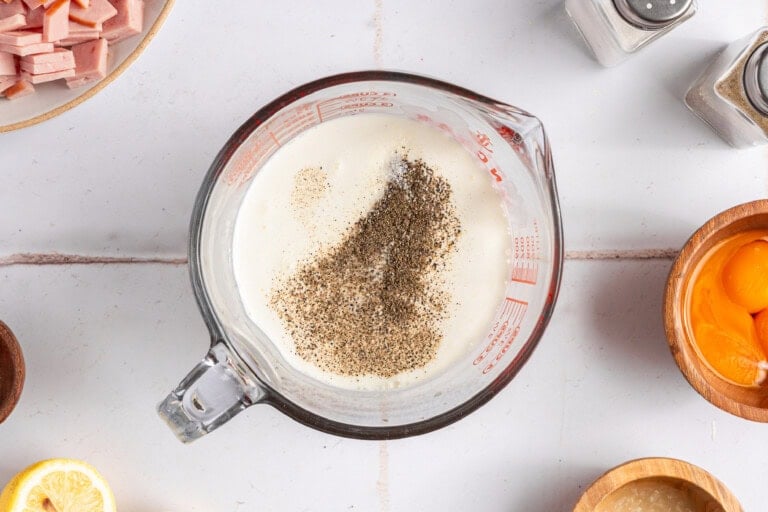 Eggs, cream, salt, and pepper for making quiche in a large mixing cup.