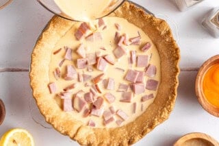 Pouring egg over diced up ham in a baked pie crust.