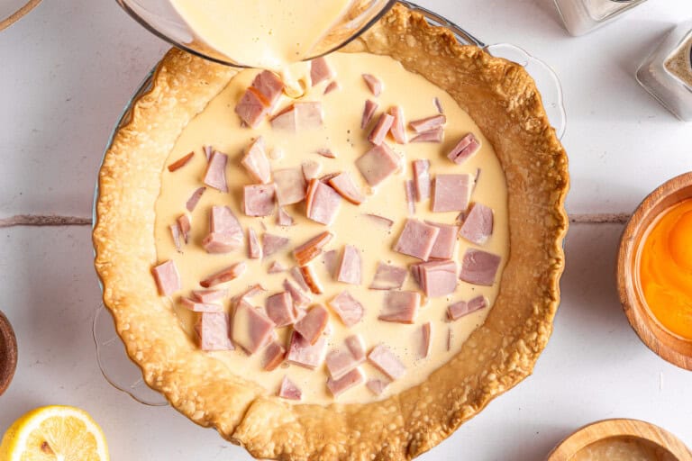Pouring egg over diced up ham in a baked pie crust.