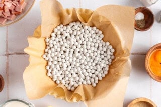 Pie dish with crust lined with parchment paper and filled with pie weights.