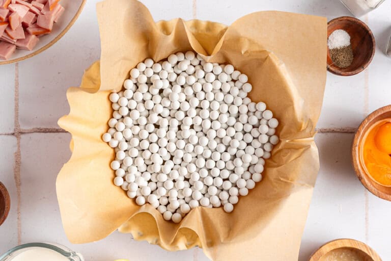 Pie dish with crust lined with parchment paper and filled with pie weights.