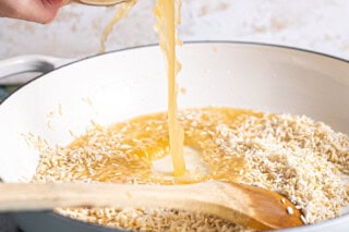 Adding broth to rice in a skillet.