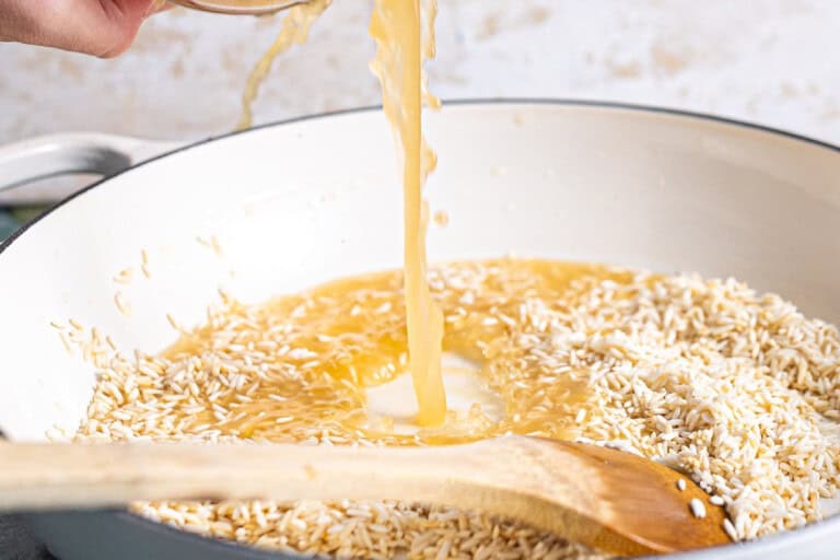 Adding broth to rice in a skillet.