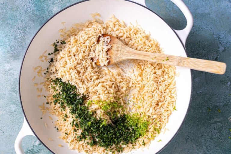 Adding cilantro and lime to cooked rice in a skillet.