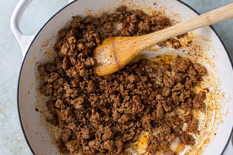 A pan with ground pork and a wooden spoon