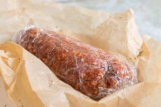 Chorizo wrapped in plastic sitting on top of a brown paper