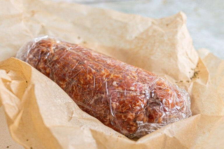 Chorizo wrapped in plastic sitting on top of a brown paper
