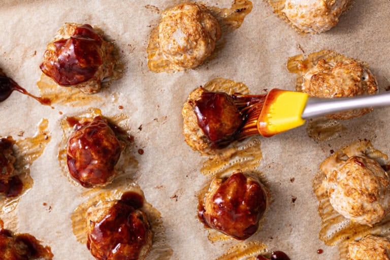 Brushing baked chicken meatballs with bbq sauce.