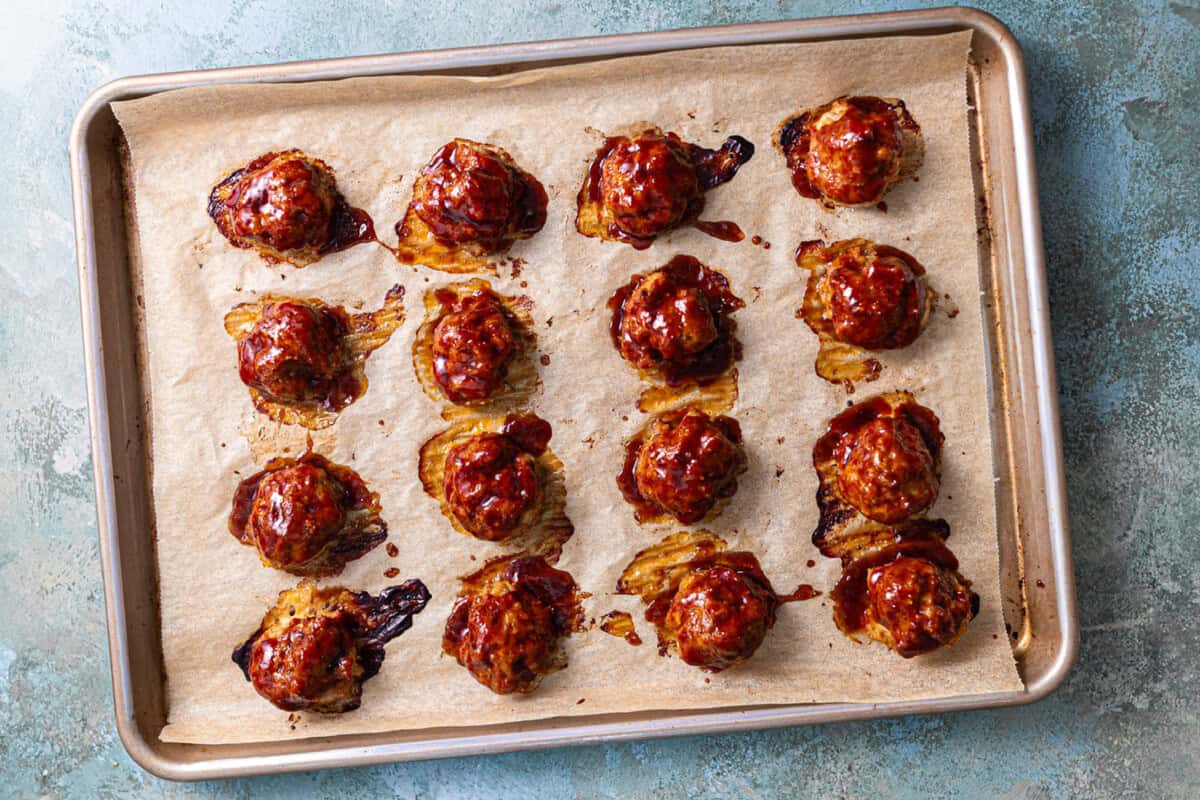 Baked meatballs with BBQ sauce on a baking sheet lined with parchment paper. 