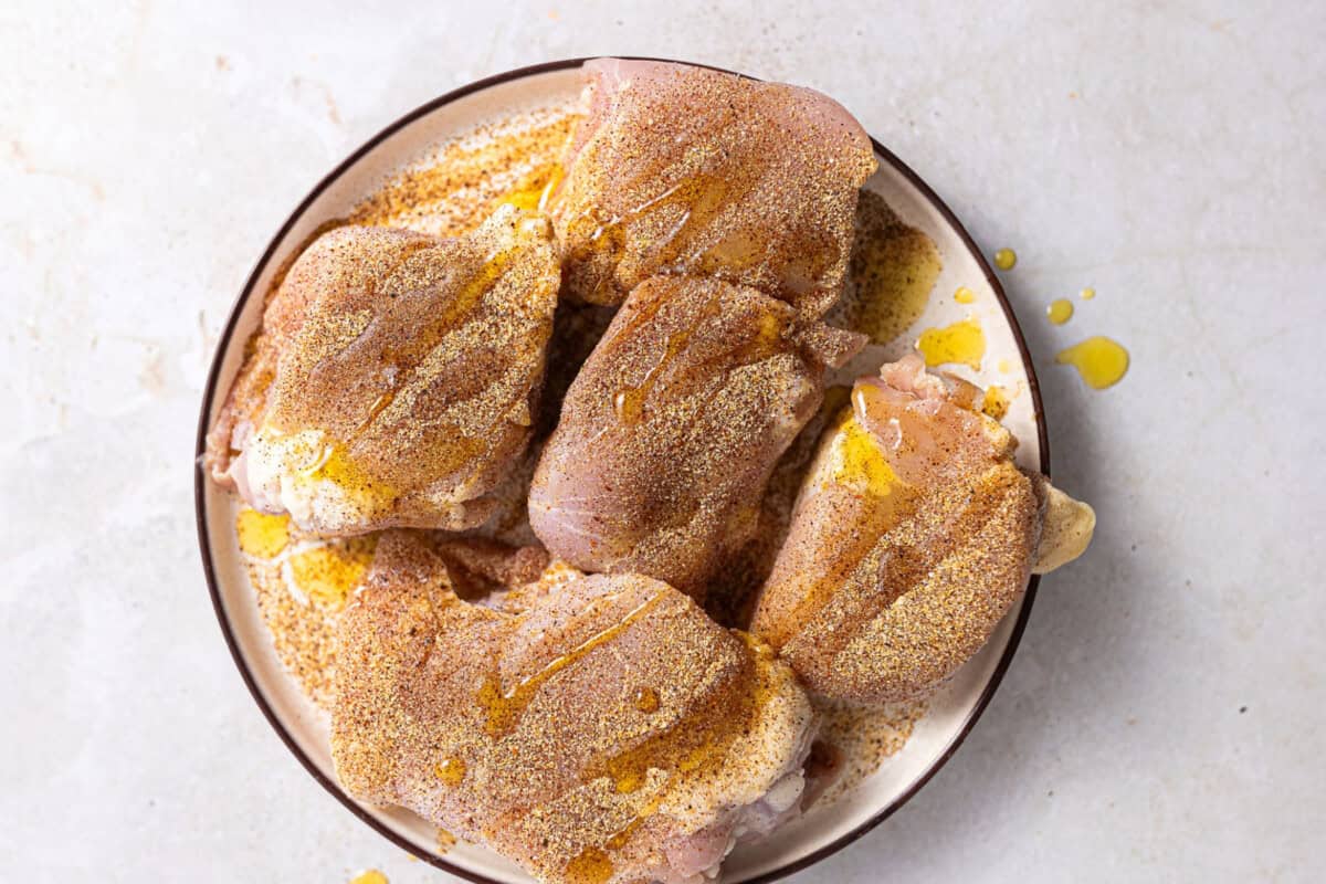 Chicken thighs coated with seasoning blend and drizzled with oil.