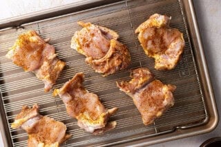Seasoned chicken thighs on a baking sheet with a wire rack.