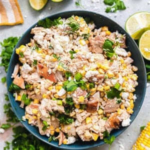 Bowl of chicken salad made with Mexican street corn surrounded by lime wedges.