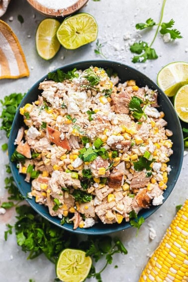 Bowl of chicken salad made with Mexican street corn surrounded by lime wedges.