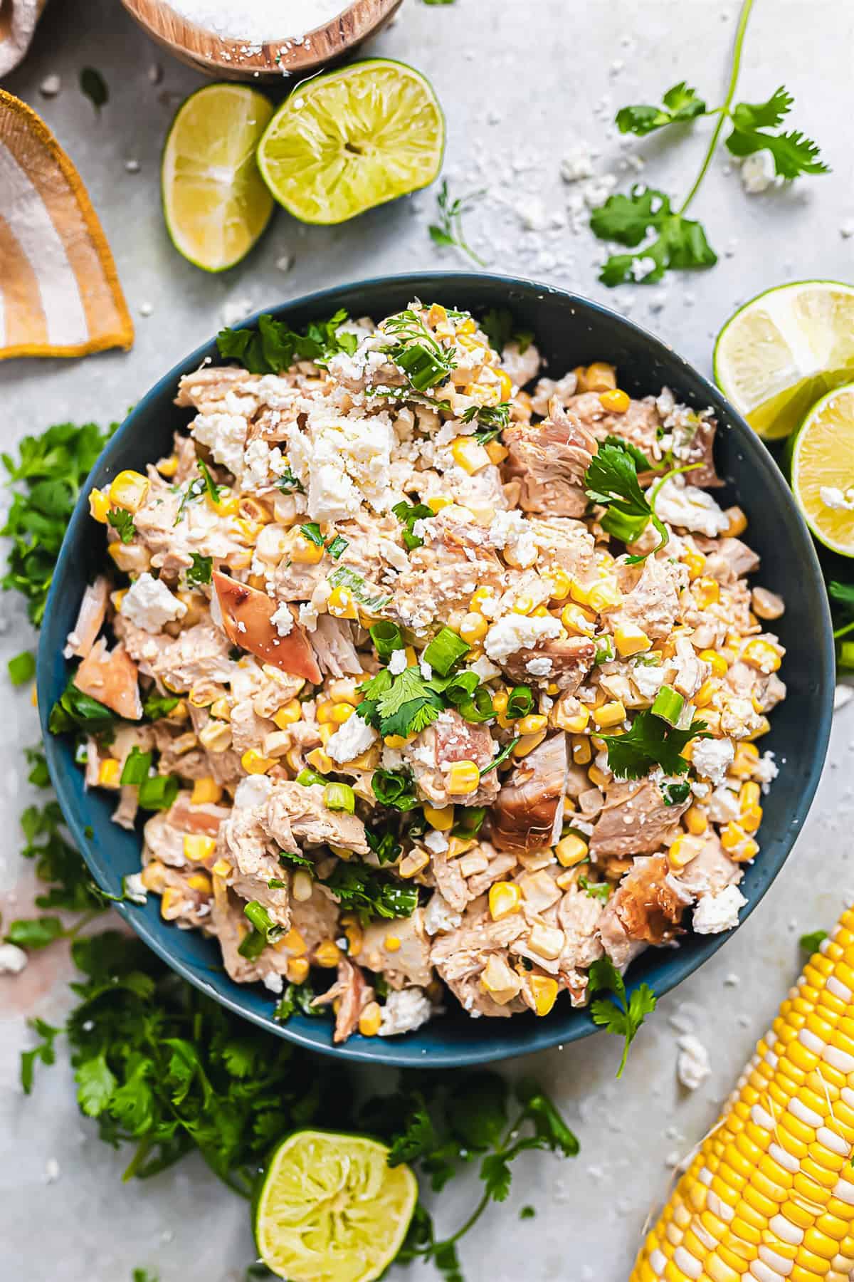 Bowl of chicken salad made with Mexican street corn surrounded by lime wedges. 