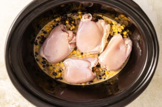 Chicken added to slow cooker with enchilada sauce to make a casserole.