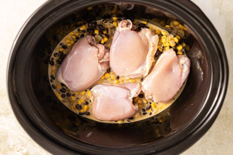 Chicken added to slow cooker with enchilada sauce to make a casserole.