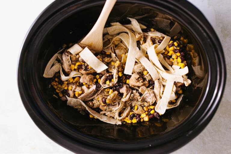 Adding tortilla strips to a slow cooker for enchilada casserole.