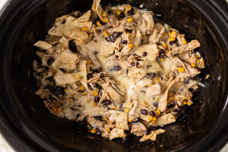 Chicken enchilada casserole topped with cheese in a slow cooker.