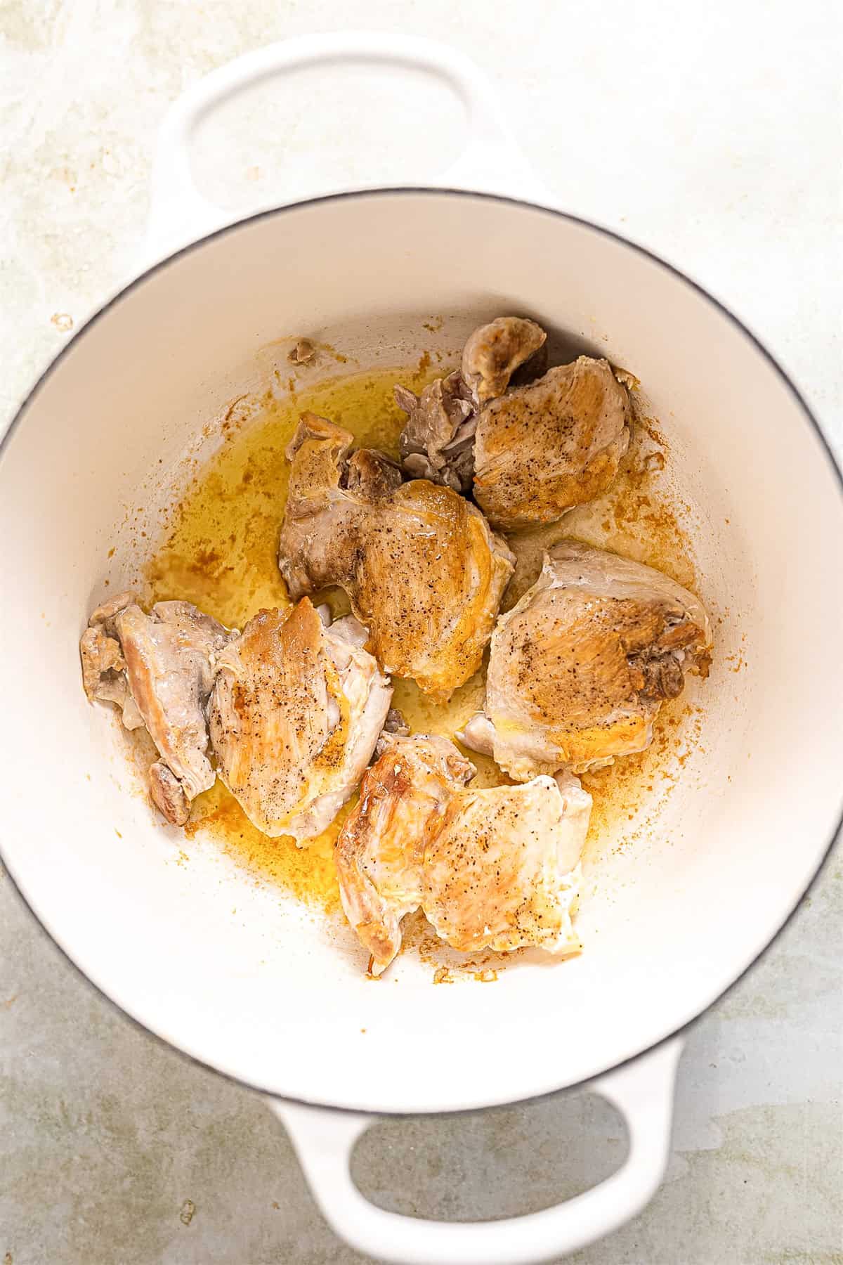 Searing chicken thighs in a white dutch oven. 