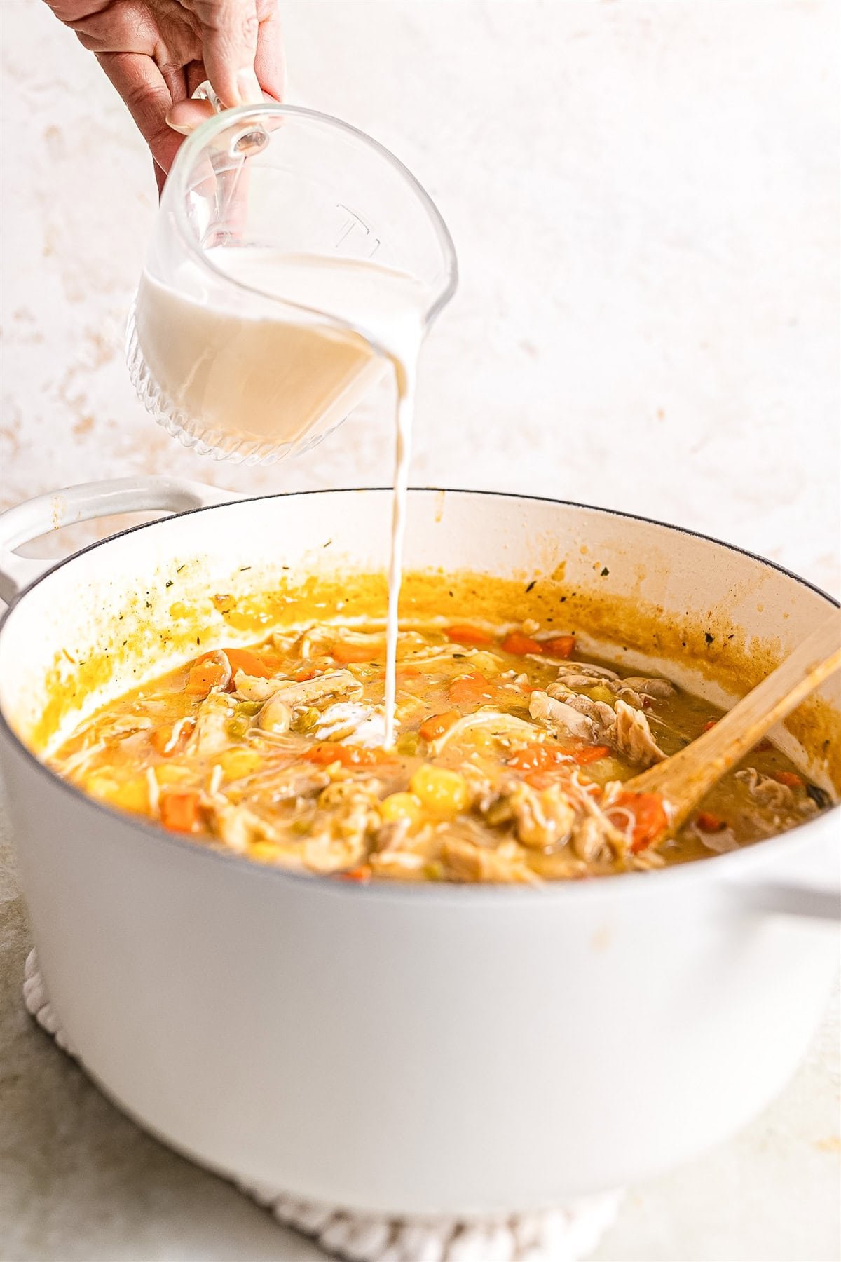 Pouring cream into pot of chicken stew. 