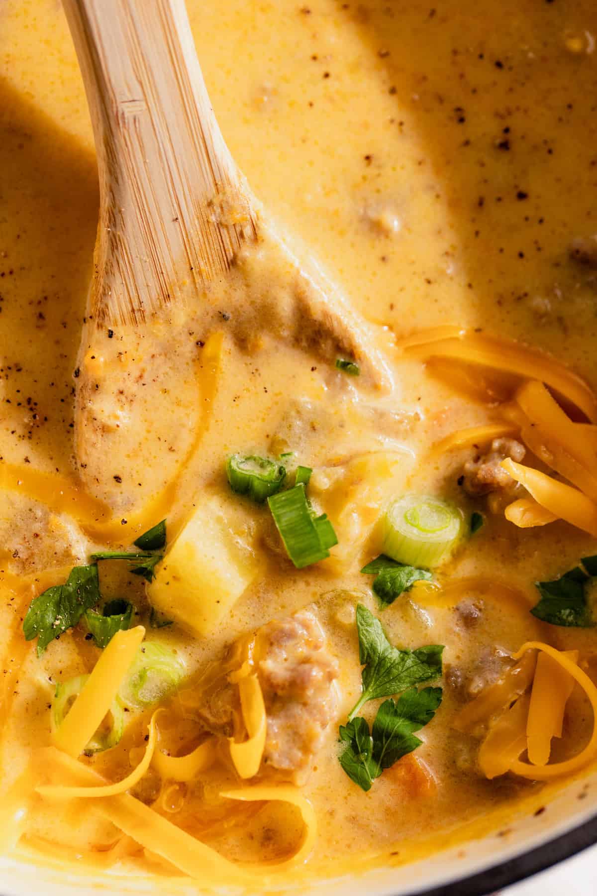 Wooden spoon serving up sausage and potato beer cheese soup.