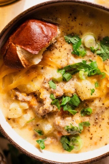 Loaded beer cheese soup in a bowl topped with parsley and green onion with a piece of pretzel bread.