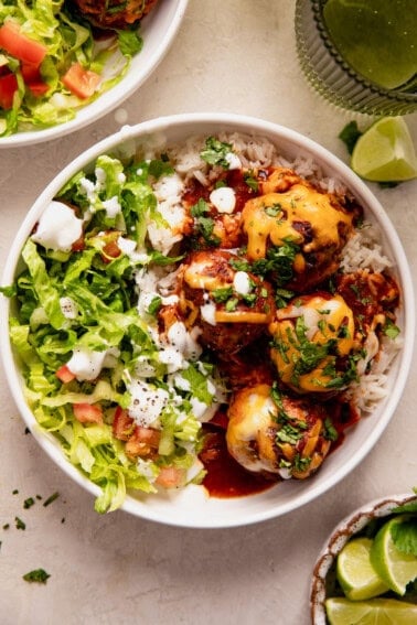 Bowl of enchilada meatballs served over rice and topped with melted cheese.