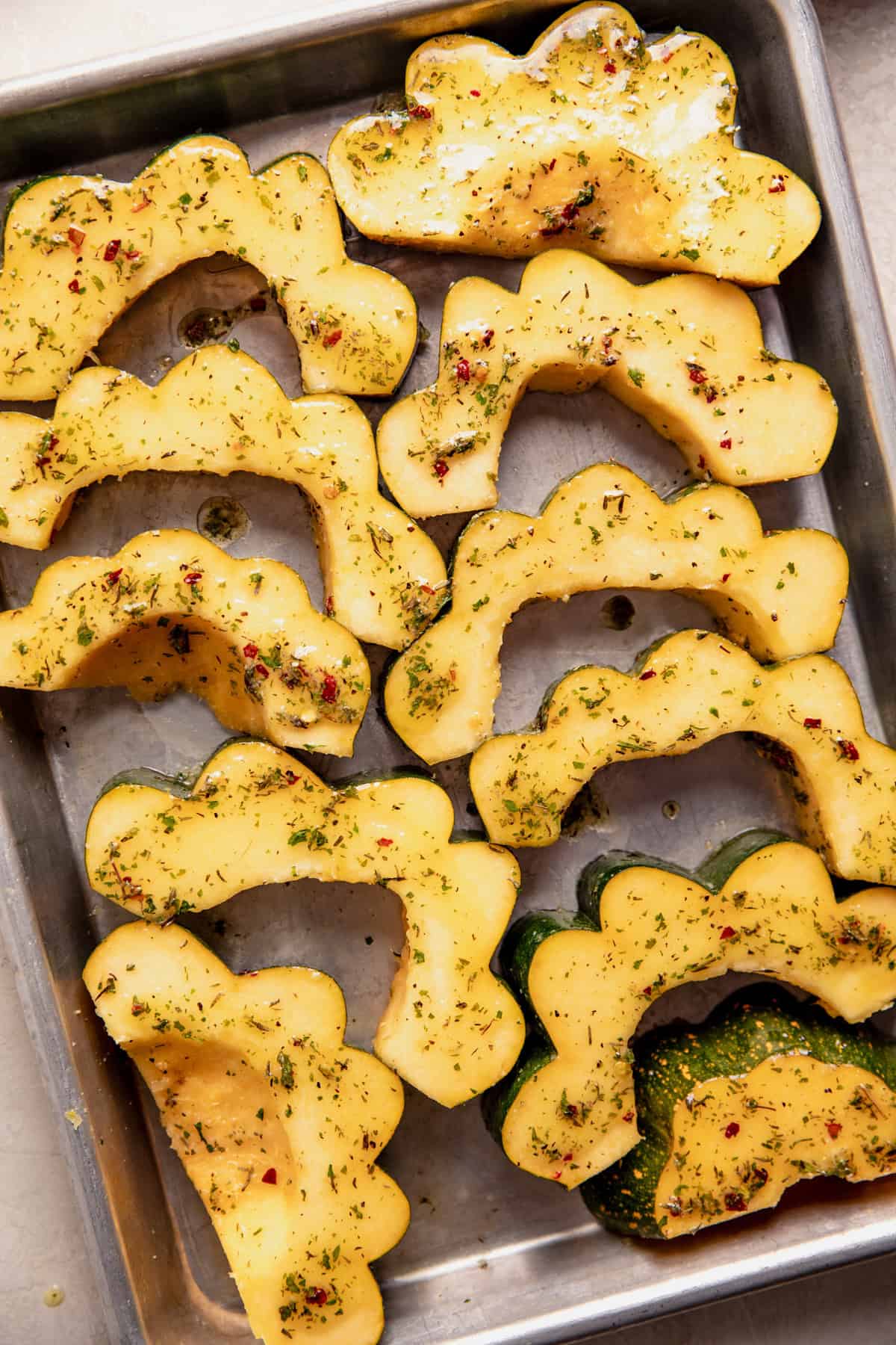 Sliced acorn squash on a baking sheet topped with oil and butter with seasonings. 