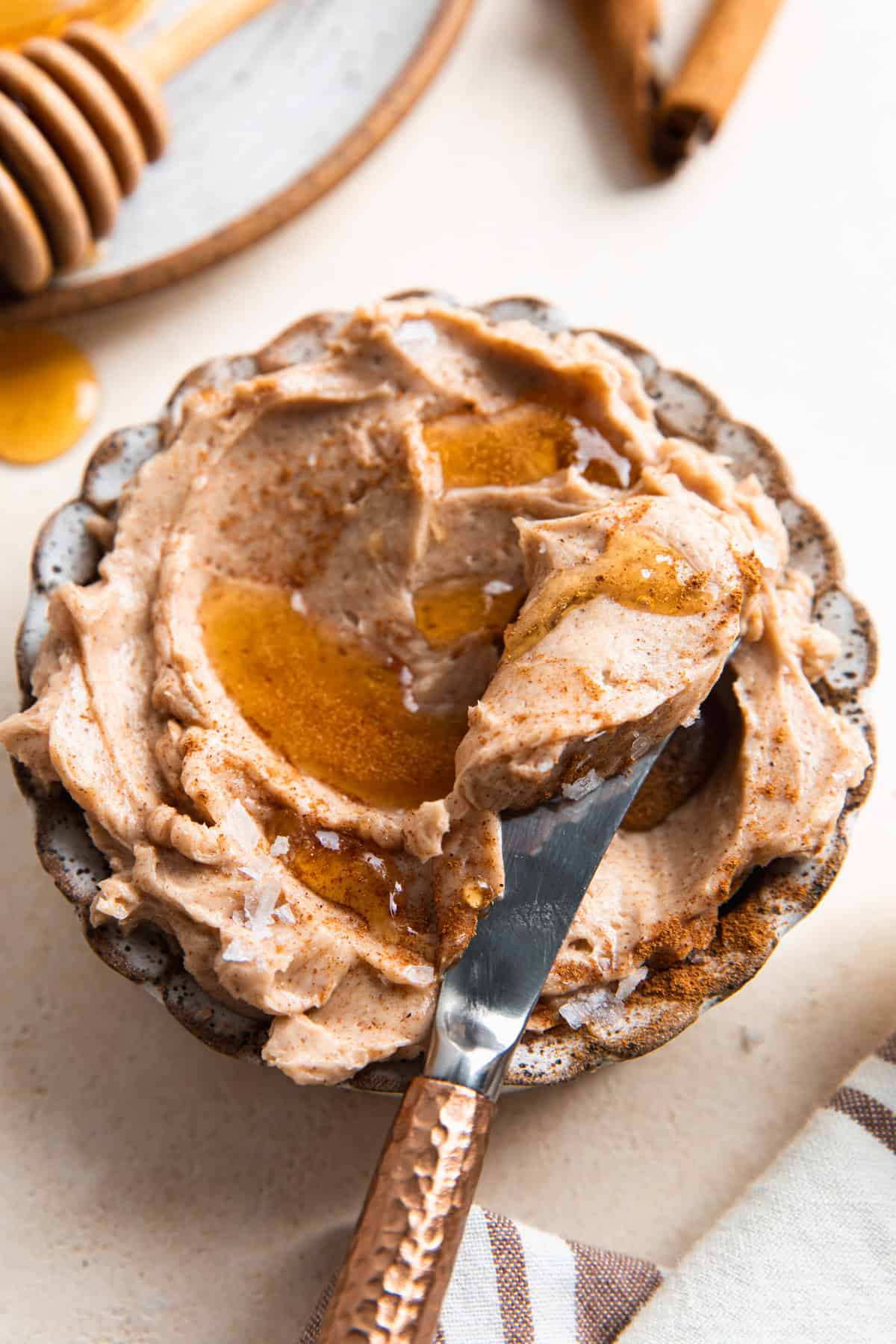Whipped cinnamon honey butter in a bowl topped with a drizzle of honey and flakey sea salt. 