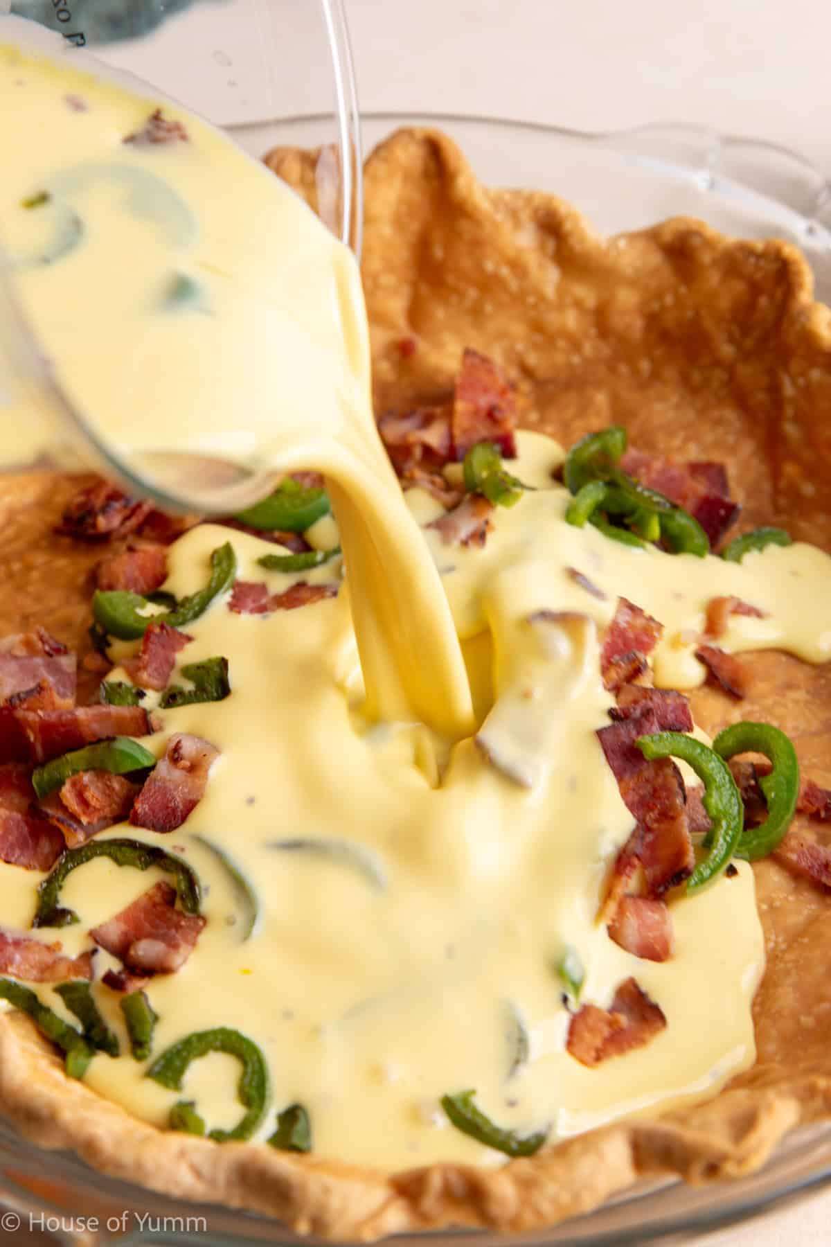 Pouring egg mixture into a pie dish with fillings for quiche.
