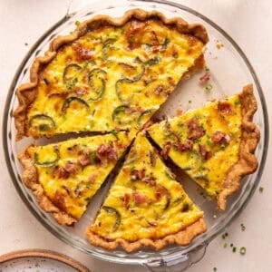 Bacon and roasted jalapeño Quiche in a pie dish sliced and topped with chives and crumbled bacon.