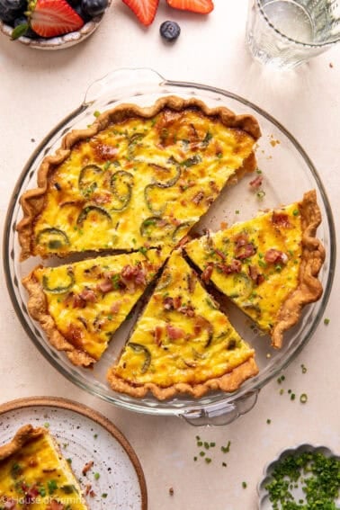 Bacon and roasted jalapeño Quiche in a pie dish sliced and topped with chives and crumbled bacon.