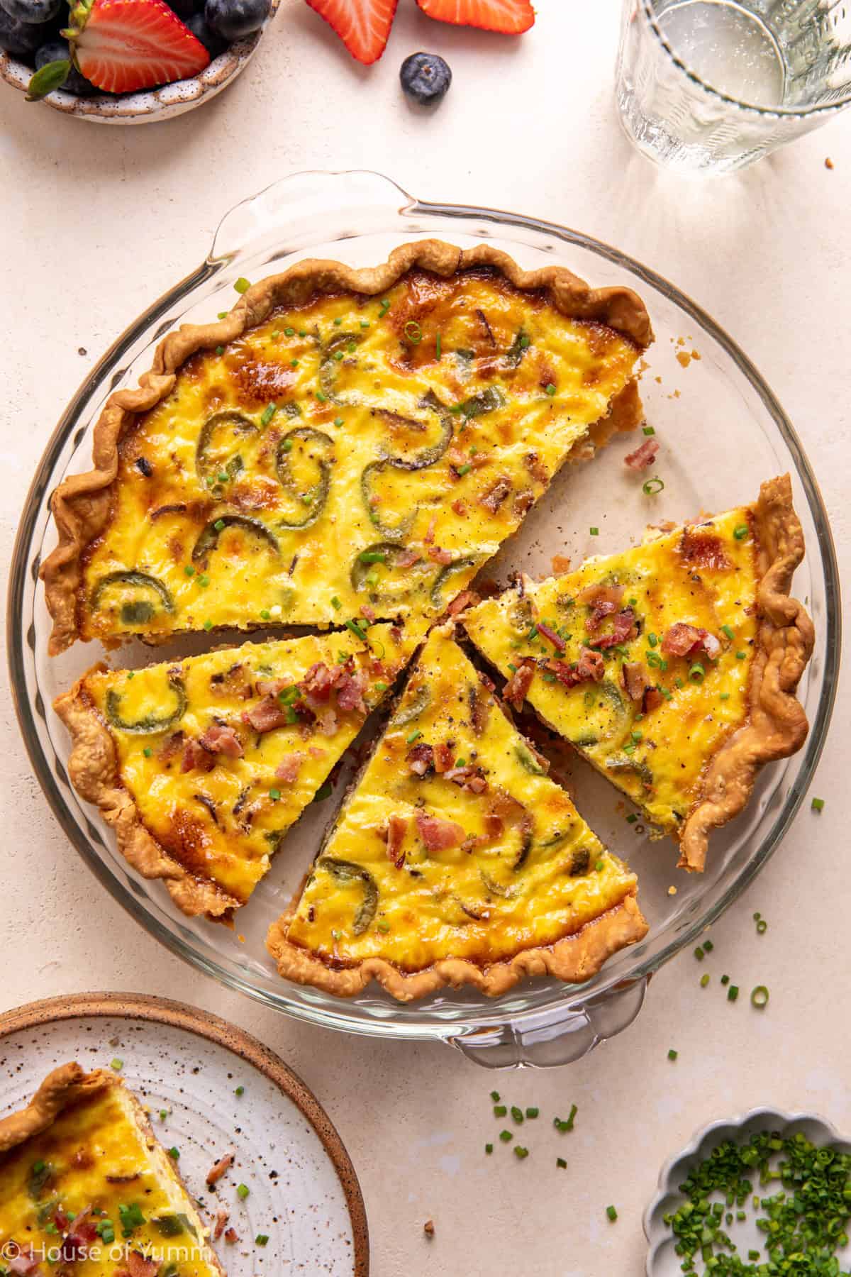 Bacon and roasted jalapeño Quiche in a pie dish sliced and topped with chives and crumbled bacon.