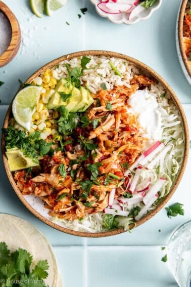 Bowl of Salsa chicken served over rice with cabbage, avocado, corn, and sour cream.