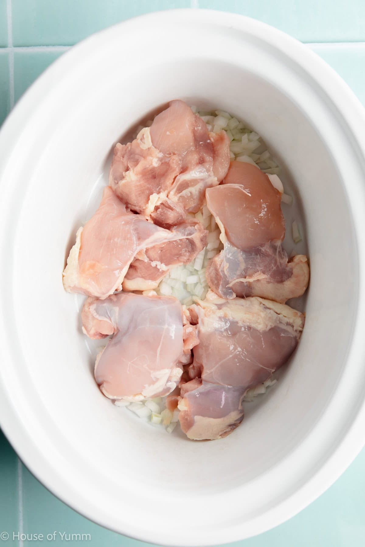 Slow cooker with onion and raw chicken.