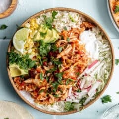 Bowl of Salsa chicken served over rice with cabbage, avocado, corn, and sour cream.