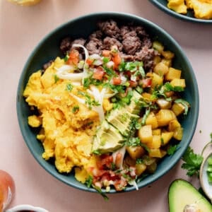 Breakfast burrito bowl made with scrambled eggs, sausage, and potatoes, topped with avocado and salsa.