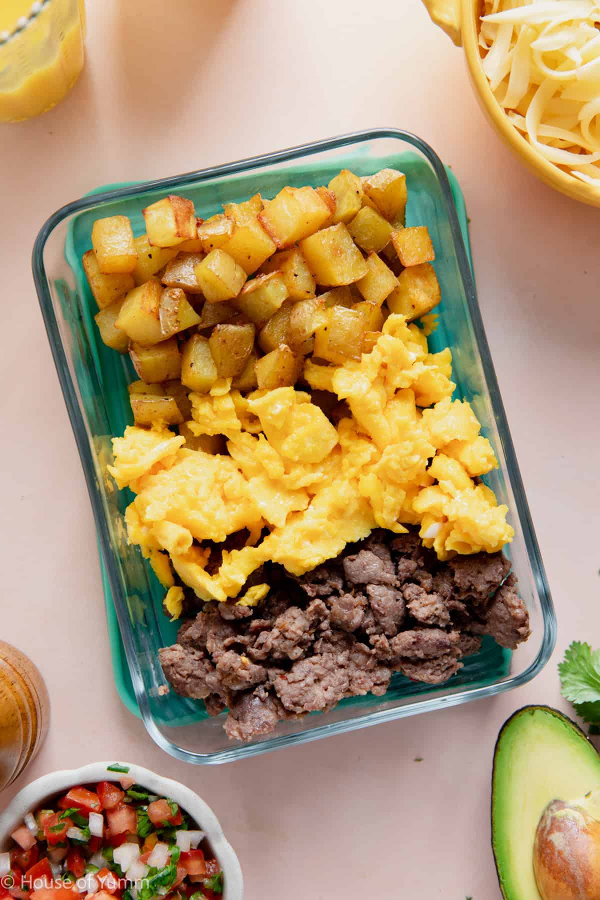 Meal prep breakfast bowls showing potatoes, eggs, and sausage in a to go glass container.