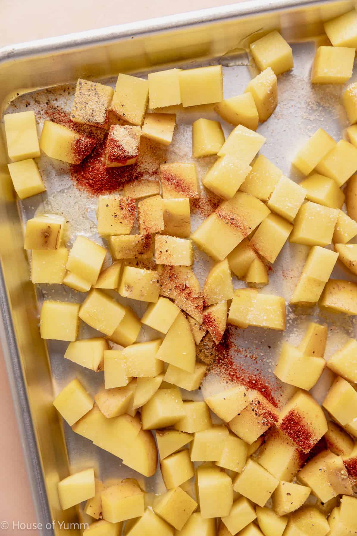 Cubed potatoes on a baking sheet drizzled with oil and sprinkled with seasonings.