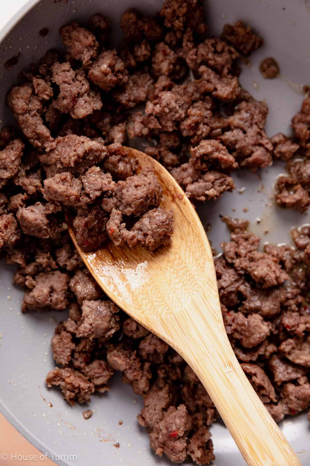 Cooked sausage in a skillet with a wooden spoon.
